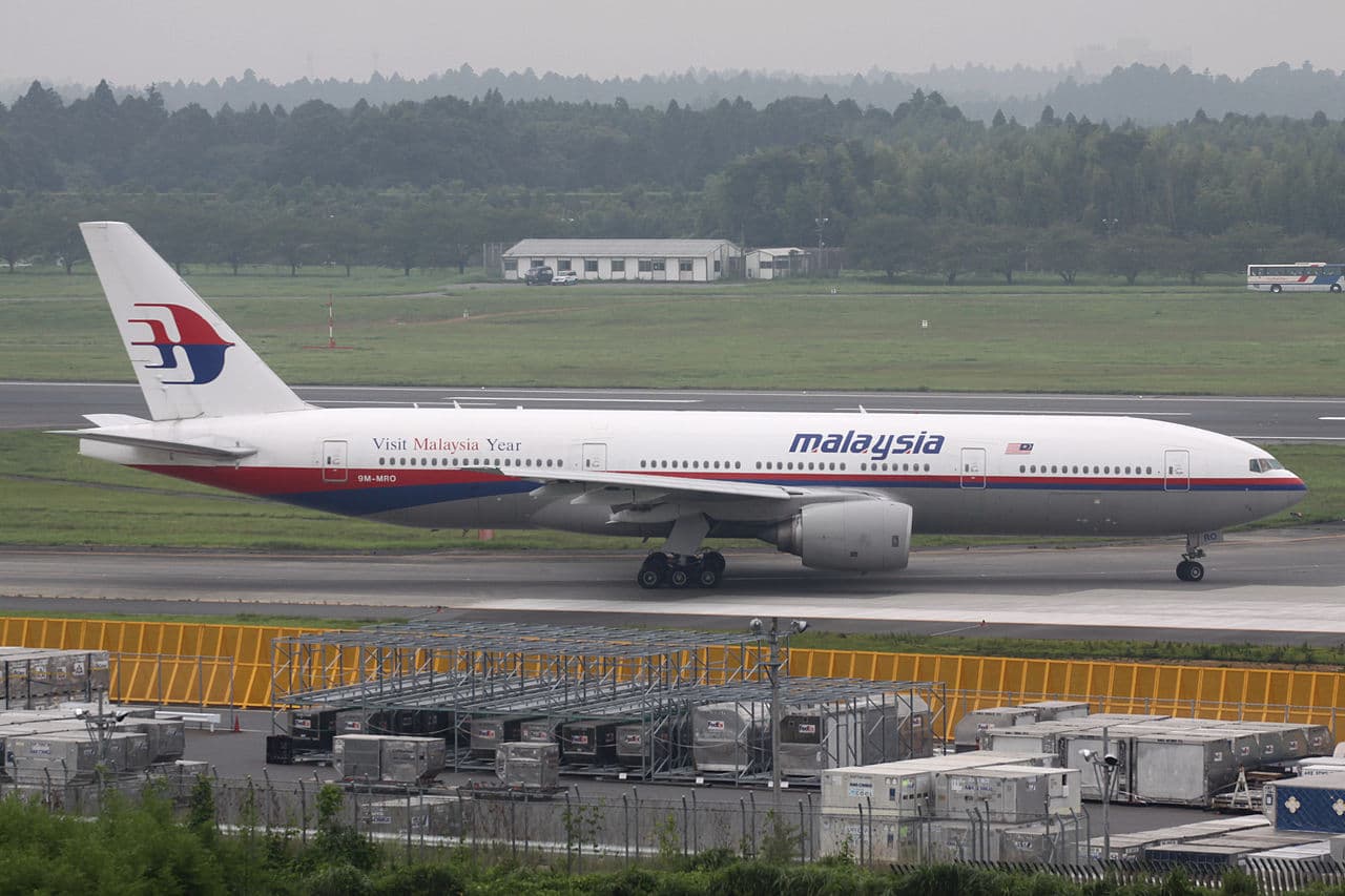 Malaysia Airlines aircraft at Kuala Lumpur International Airport with security personnel near boarding gate