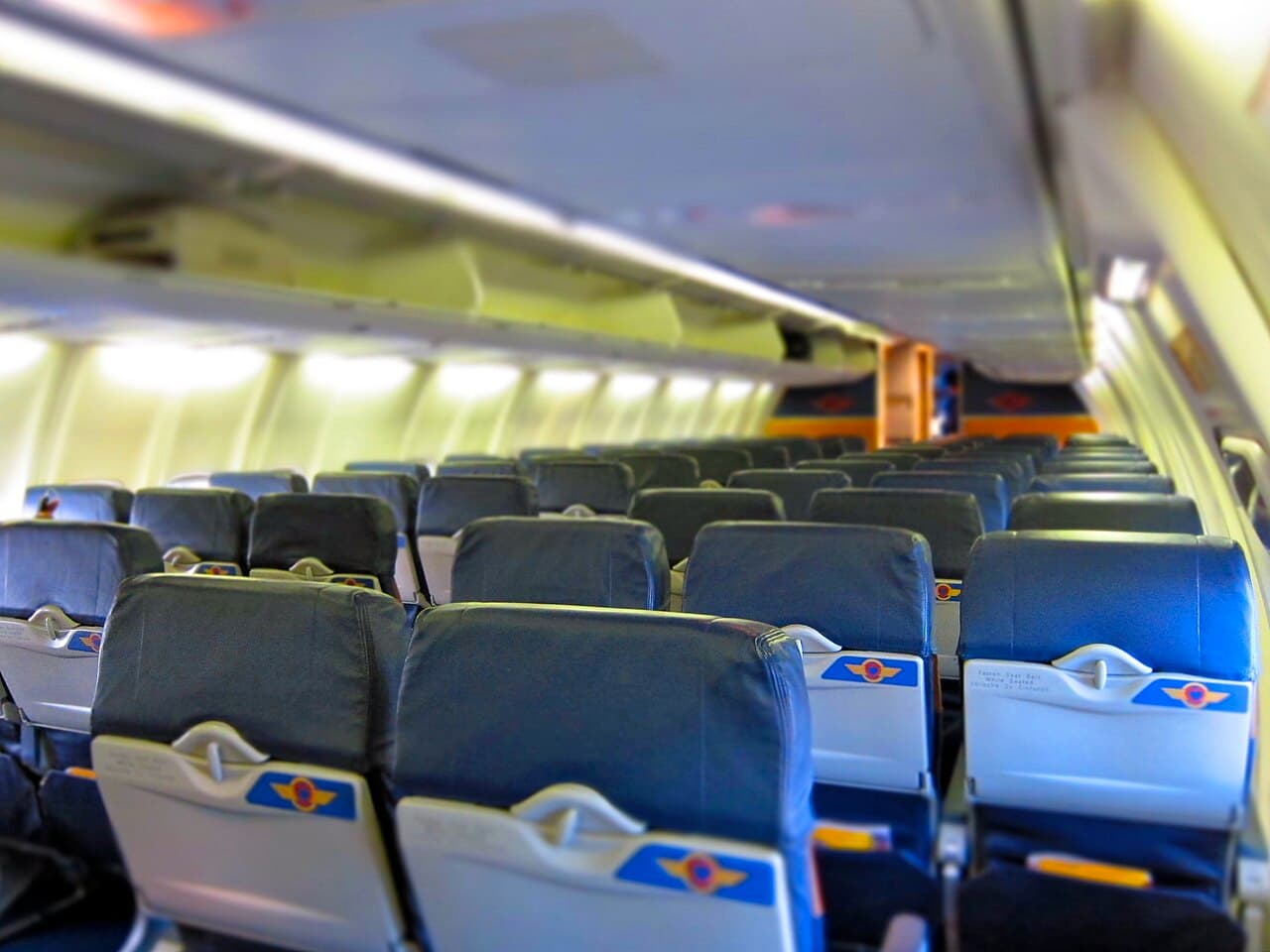 Commercial aircraft interior with seat rows and cabin crew walking past passengers