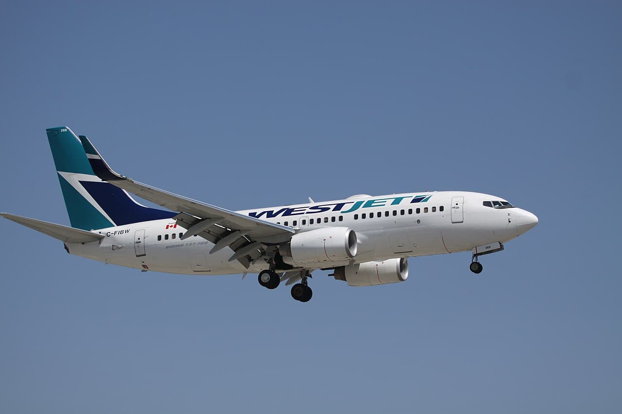 WestJet aircraft parked at airport gate under cloudy sky with flight attendants walking nearby